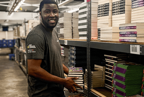 What We Offer - Image 2 "Smiling warehouse employee holding books in front of shelves."